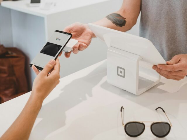 Hände halten ein Smartphone über einem Bezahlterminal